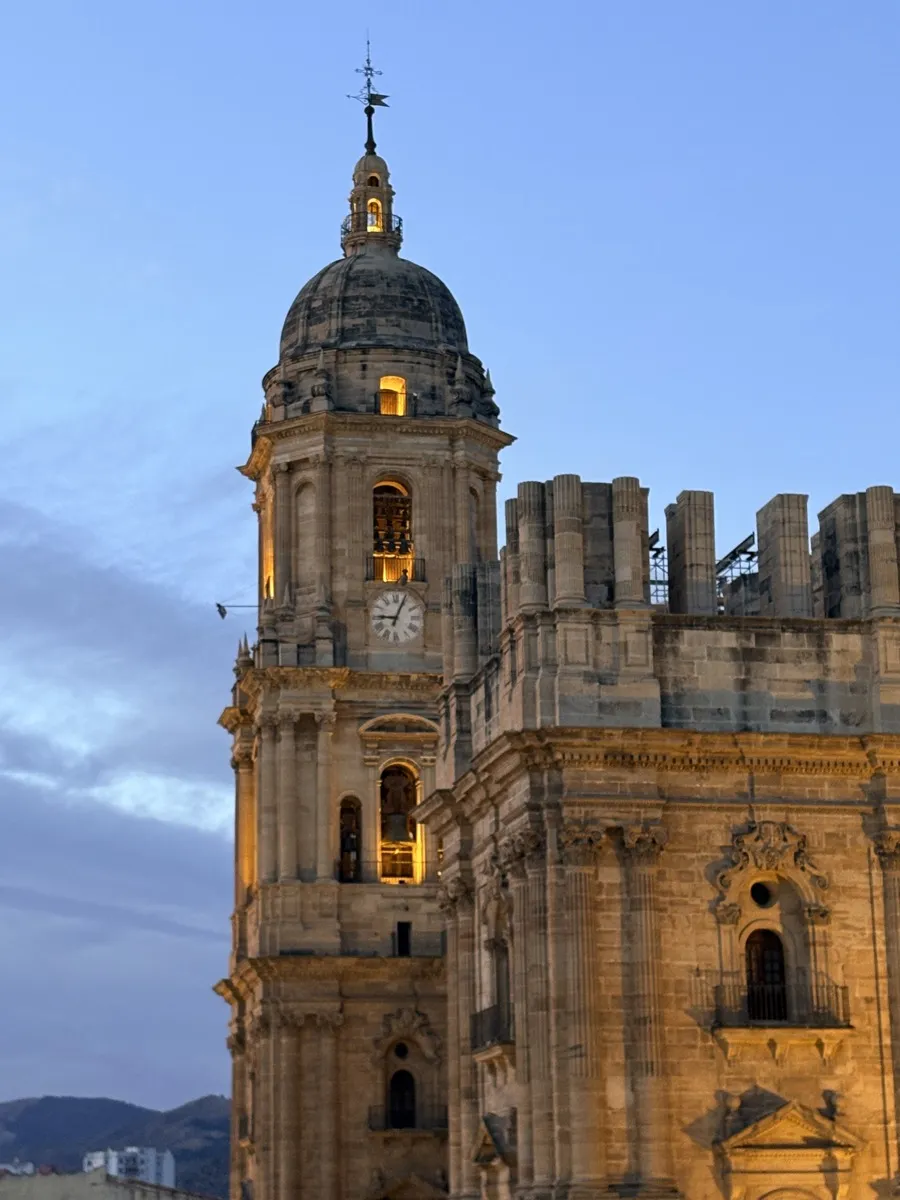 Close-up of Málaga Cathedral's bell tower stonework and clock lit gold at dusk