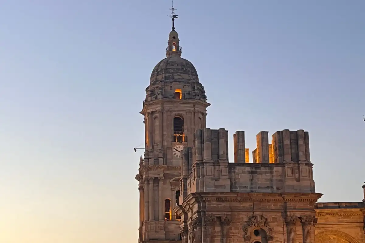 Málaga Cathedral tower lit by golden sunset light against a pale blue sky