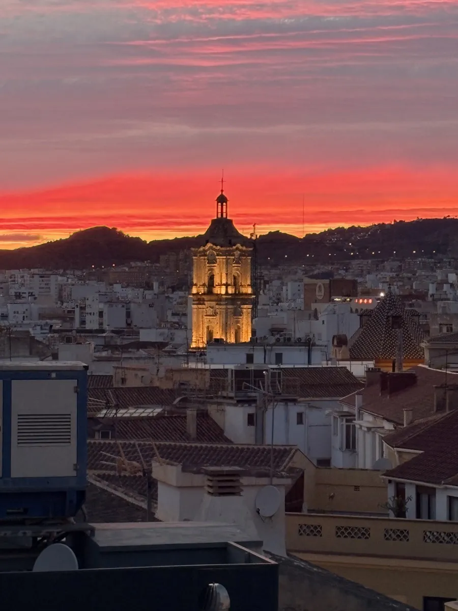 Málaga Cathedral tower glowing at sunset with the hills behind the city