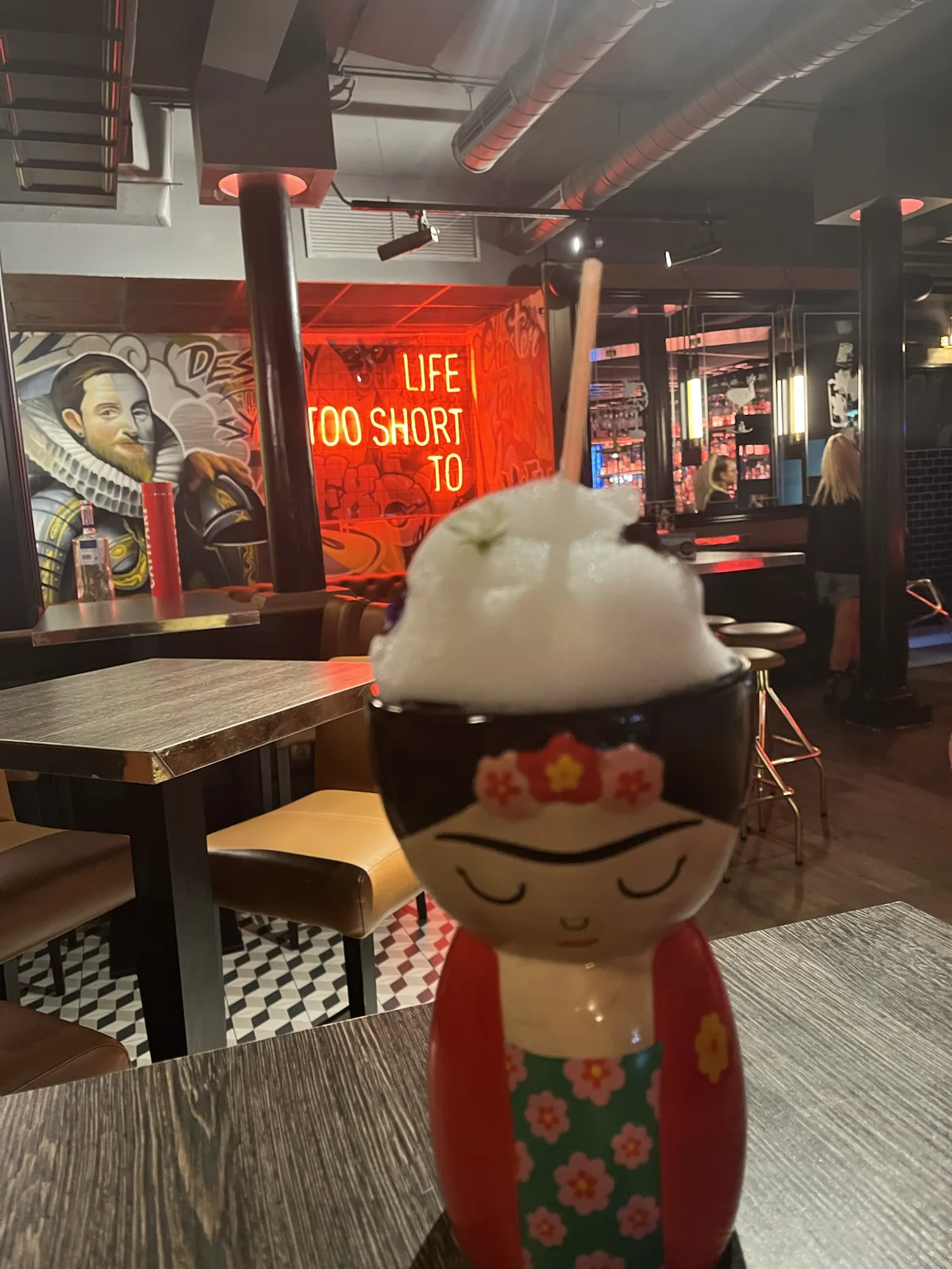 A cocktail served in a Frida Kahlo mug under a cloud of candy floss at Chester & Punk, the neon sign and street-art mural of the Punk side behind it