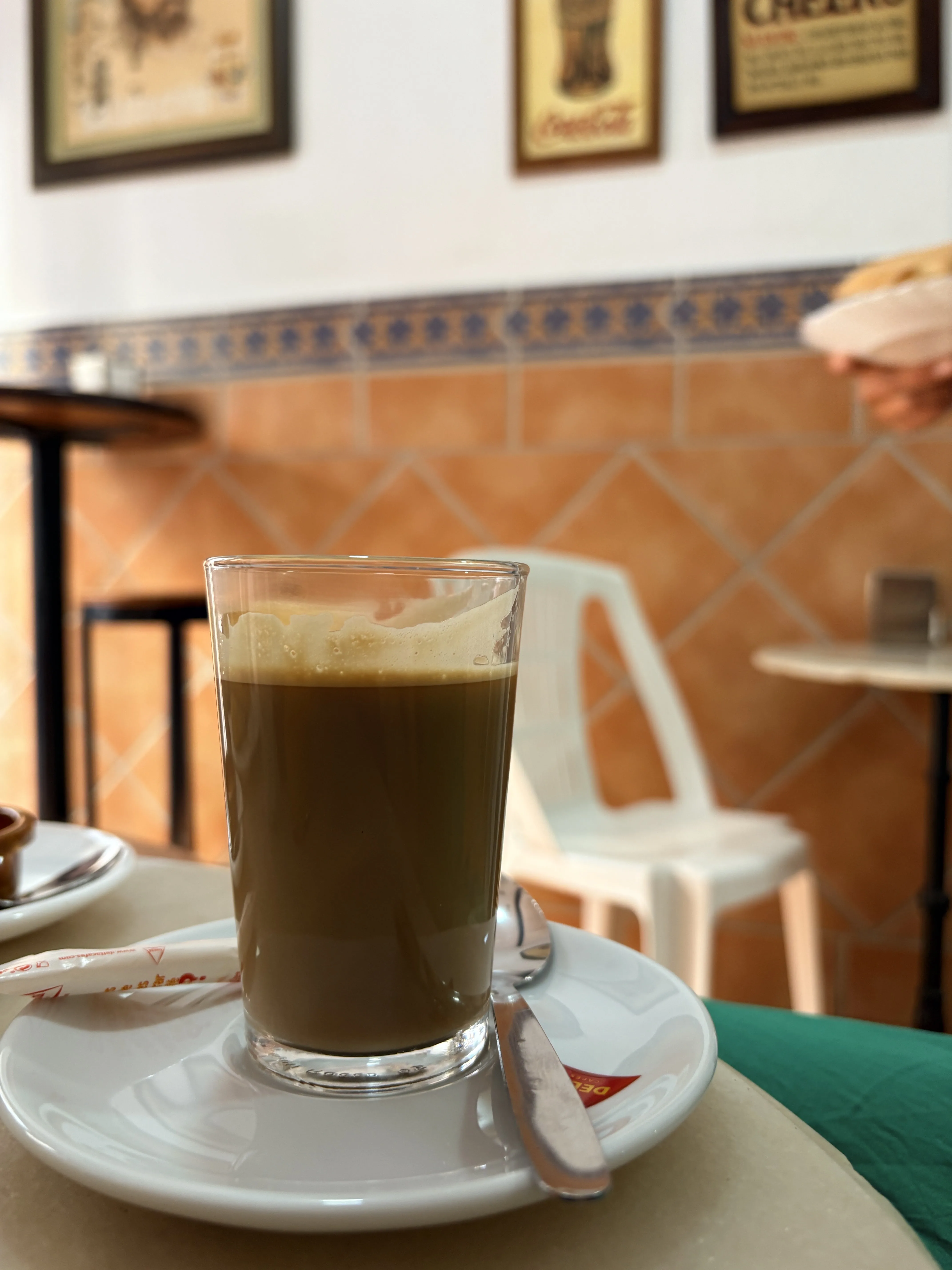 A glass of coffee on a saucer at a traditional tiled café table in Málaga