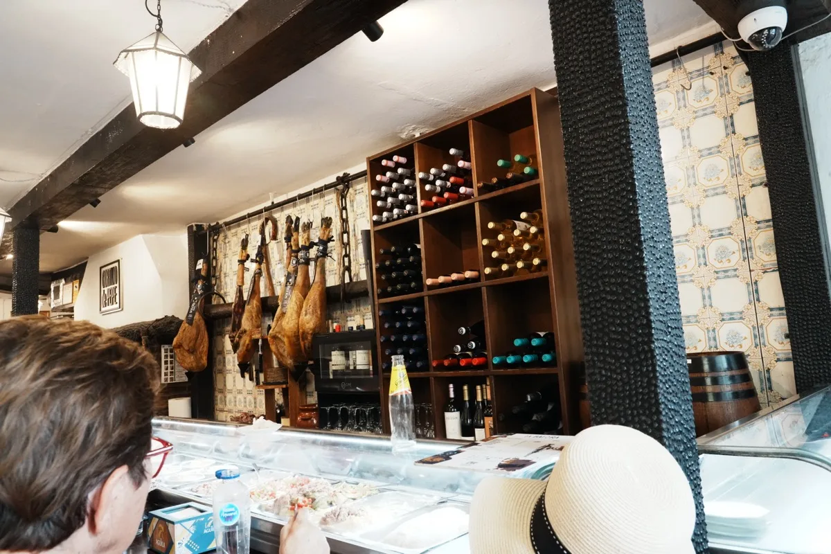 Trays of cold tapas in a glass case on the bar at Cortijo de Pepe, hams hanging above and a rack of wine bottles behind