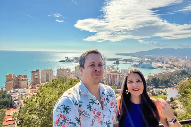 Couple posing at a Málaga hilltop viewpoint with the port and Mediterranean sea behind them