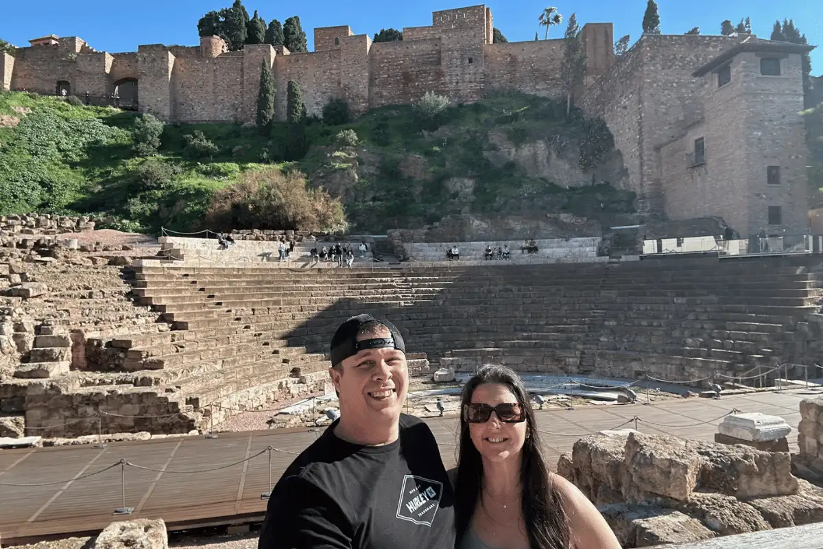 A man and a woman smiling in front of the Roman Theatre and the Alcazaba in Málaga