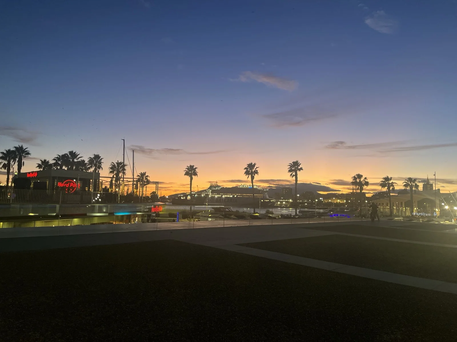 Muelle Uno at dusk, the Hard Rock Cafe sign lit, palms and a ferry across the harbour