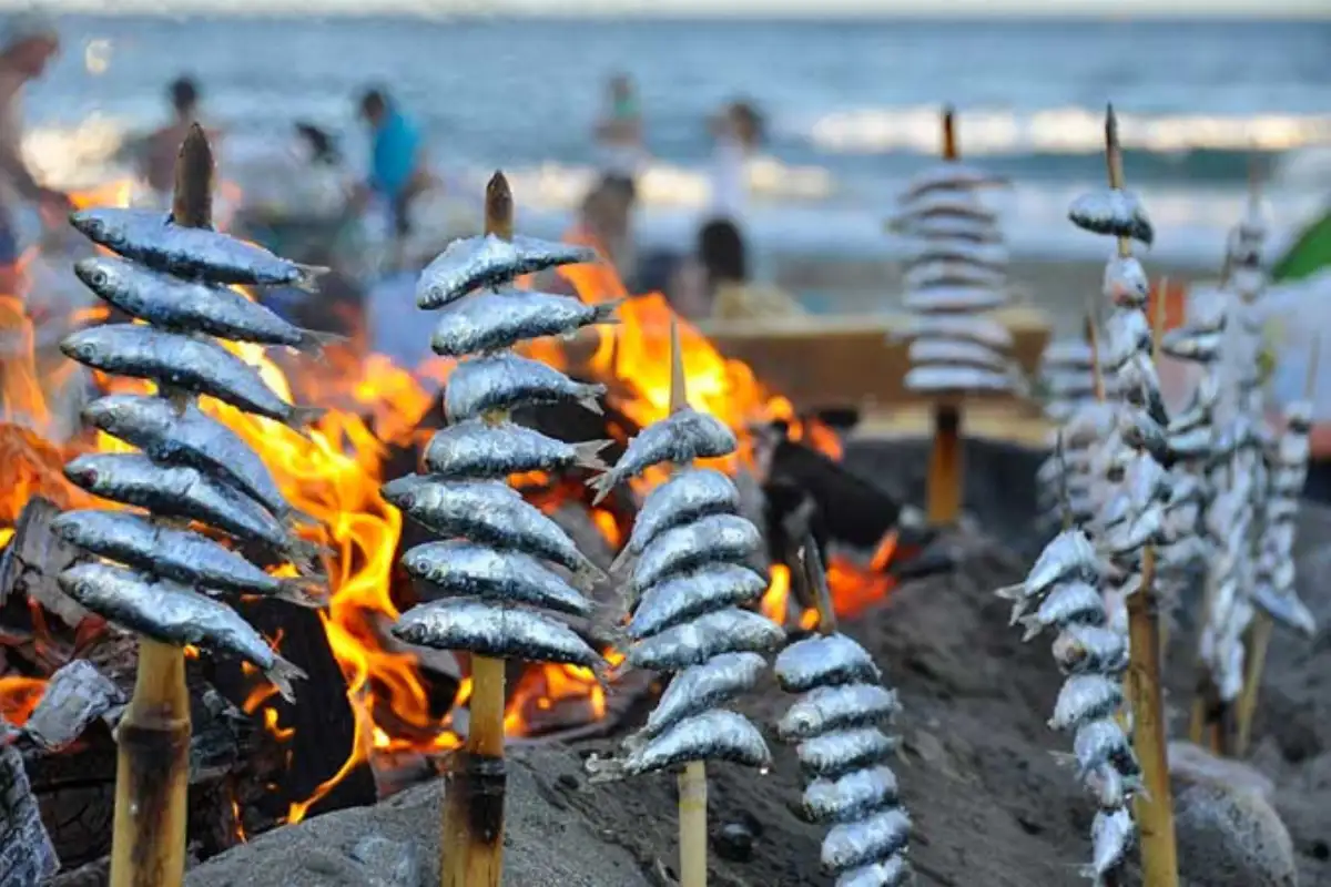 Skewers of sardines grilling over an open fire on the beach in Málaga, the classic espetos