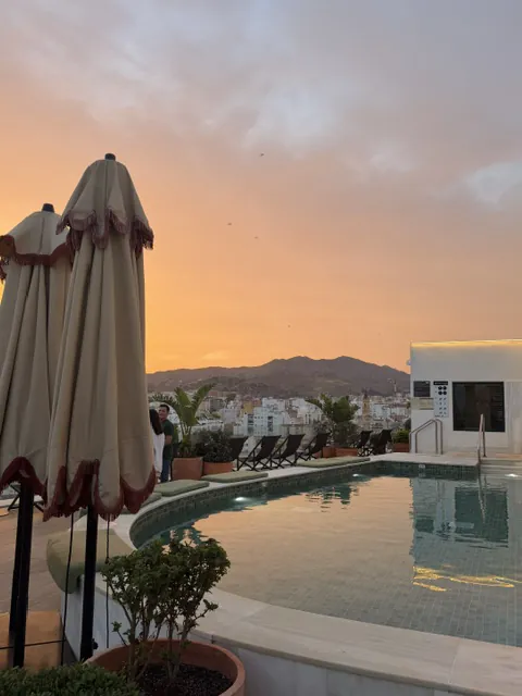 The H10 Croma rooftop pool at sunset, with its fringed parasols folded and the mountains behind Málaga turning pink