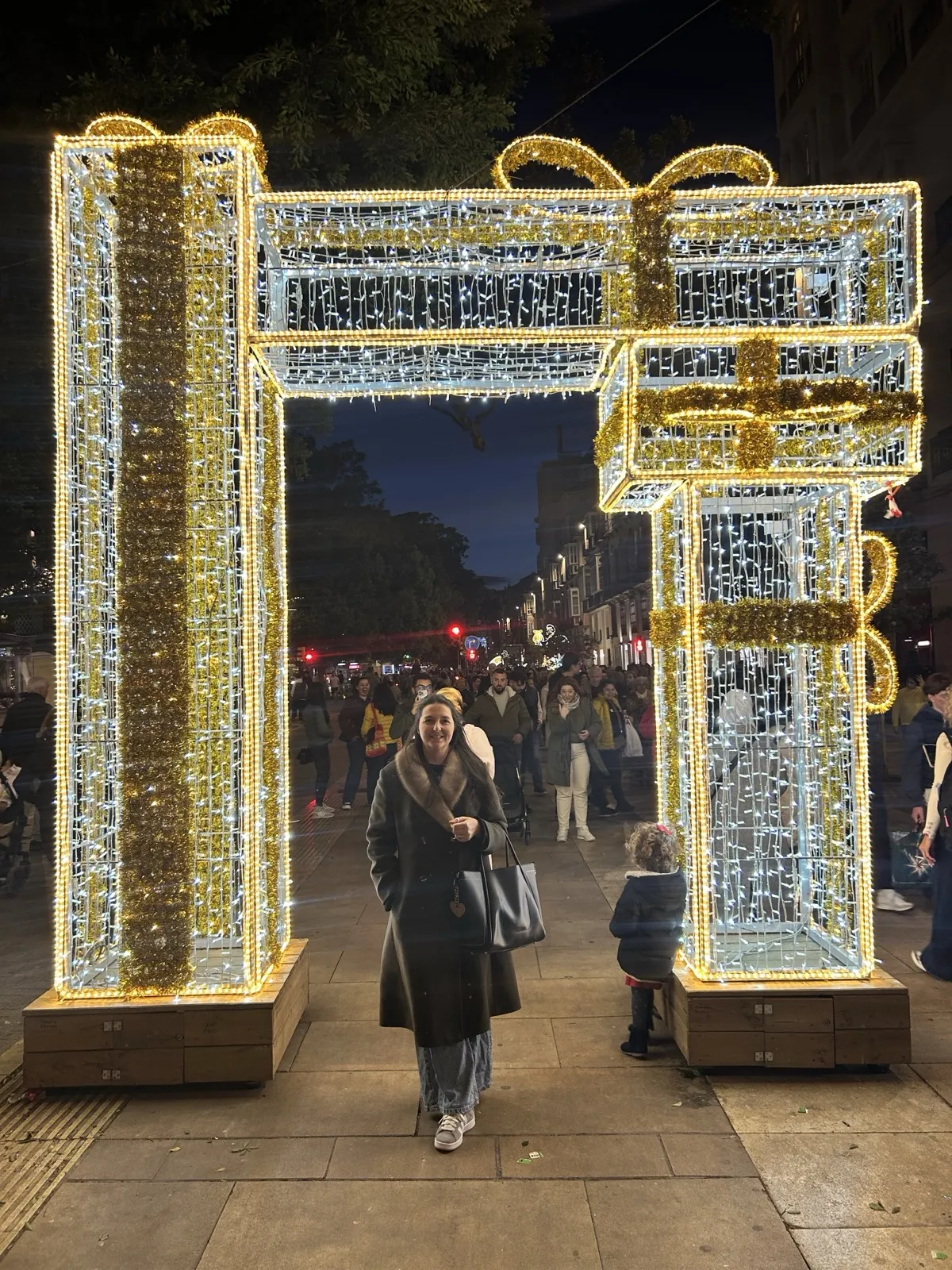 Heidi standing under a giant gift-box light arch on the Alameda in Malaga at Christmas
