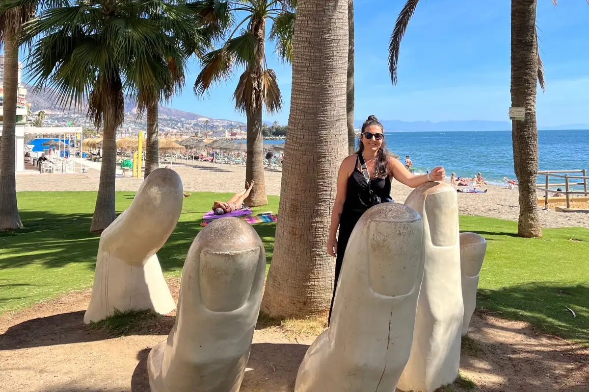 Woman posing with giant finger sculptures on Málaga beachfront in September sunshine