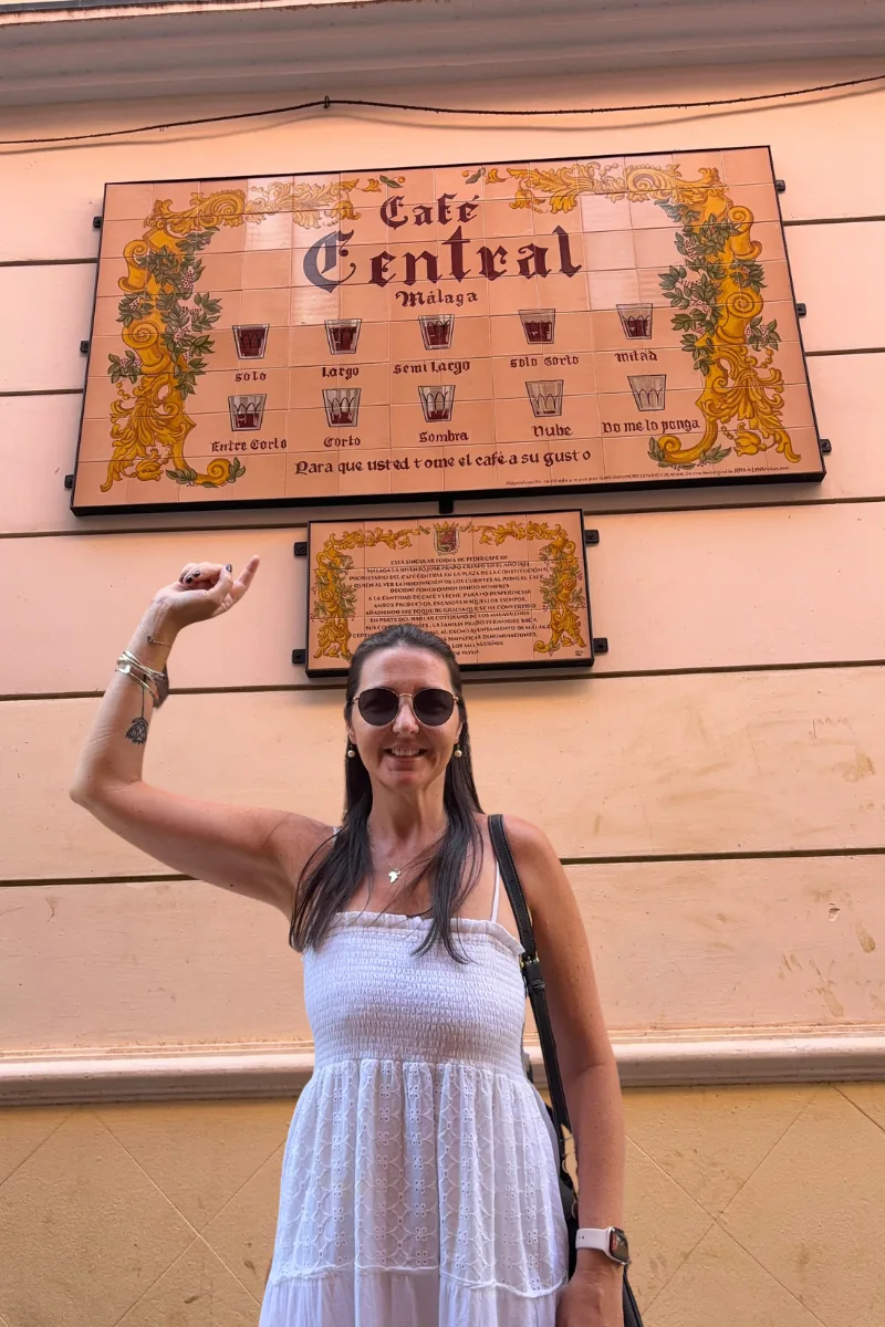 Heidi pointing up at the tiled Café Central chart in Málaga showing the ten ways to order coffee
