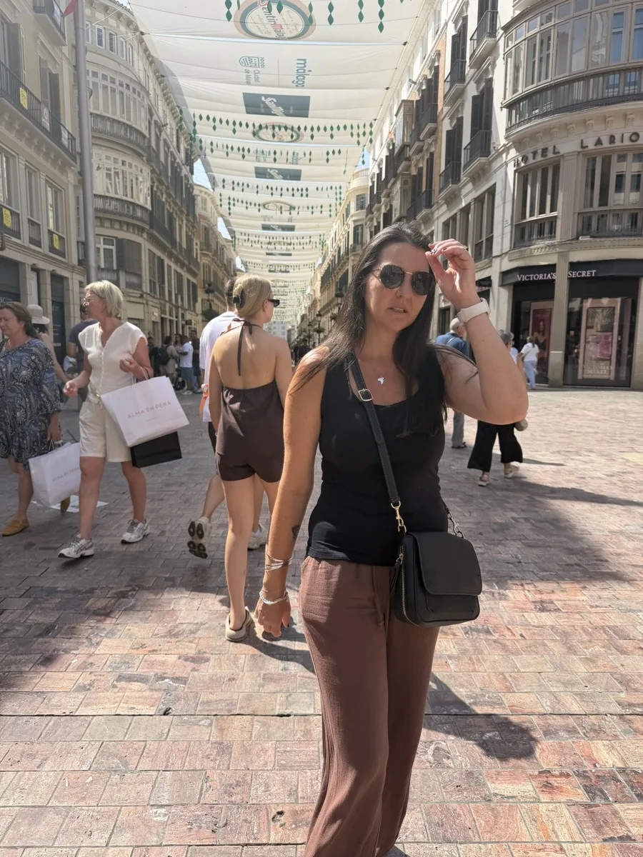 Heidi walking down Calle Larios in Málaga with a black cross-body bag zipped across her front, the crowd behind her