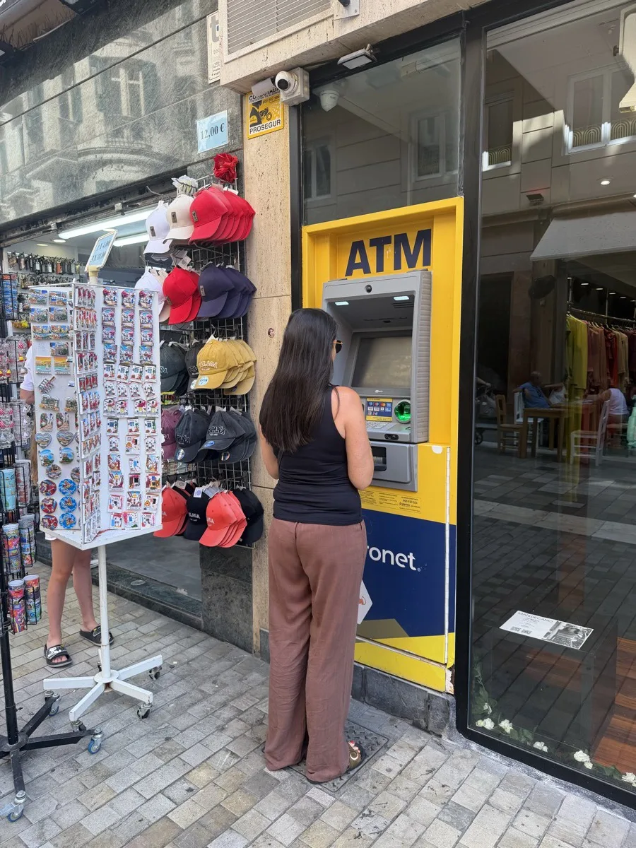 Heidi using a yellow Euronet ATM set into a shop front in Málaga, the standalone kind that charges high fees