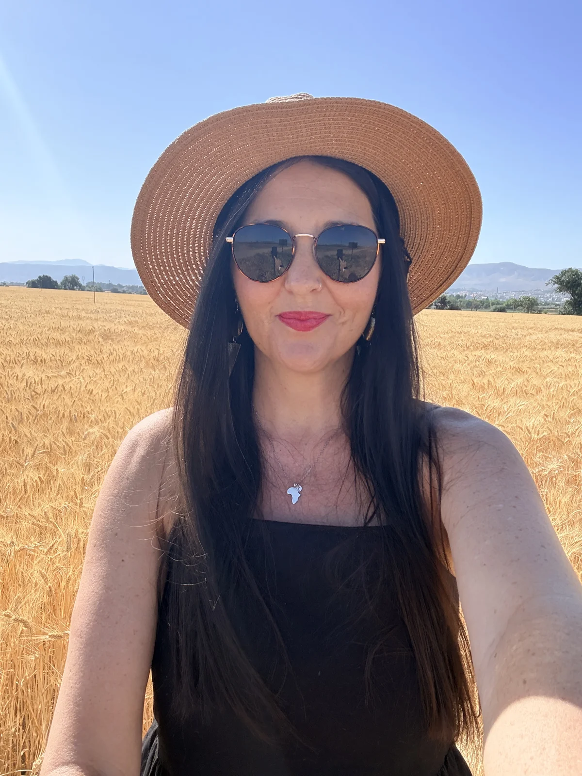 Heidi Hein in a straw hat and sunglasses, standing in a wheat field under a blue sky