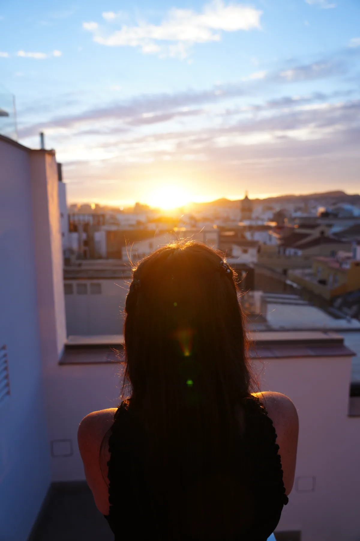Heidi from behind, silhouetted against the setting sun on the rooftop terrace of Hotel Molina Lario, with Málaga's rooftops spread out below