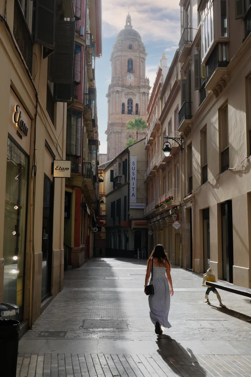Heidi walking down a narrow old-town street in Málaga towards the cathedral tower