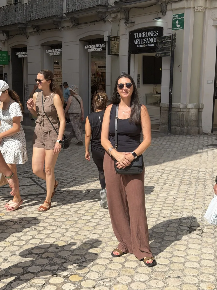 Heidi standing in a busy square in Málaga with her cross-body bag in front of her as people pass
