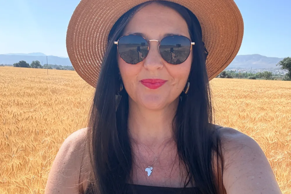 Heidi in a straw hat and sunglasses in front of a wheat field near Malaga