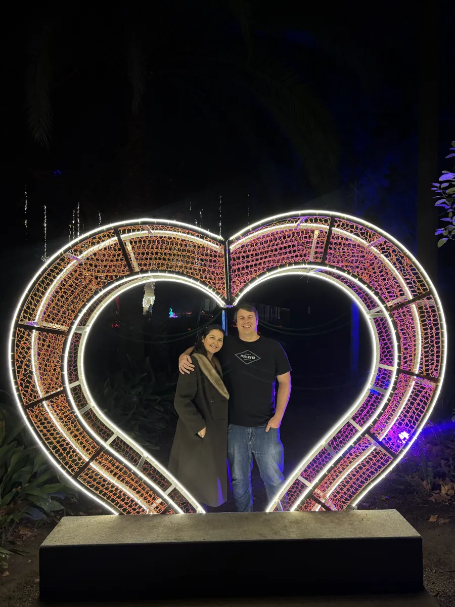 Two people posing inside a glowing heart-shaped light installation at La Concepcion's Christmas lights in Malaga