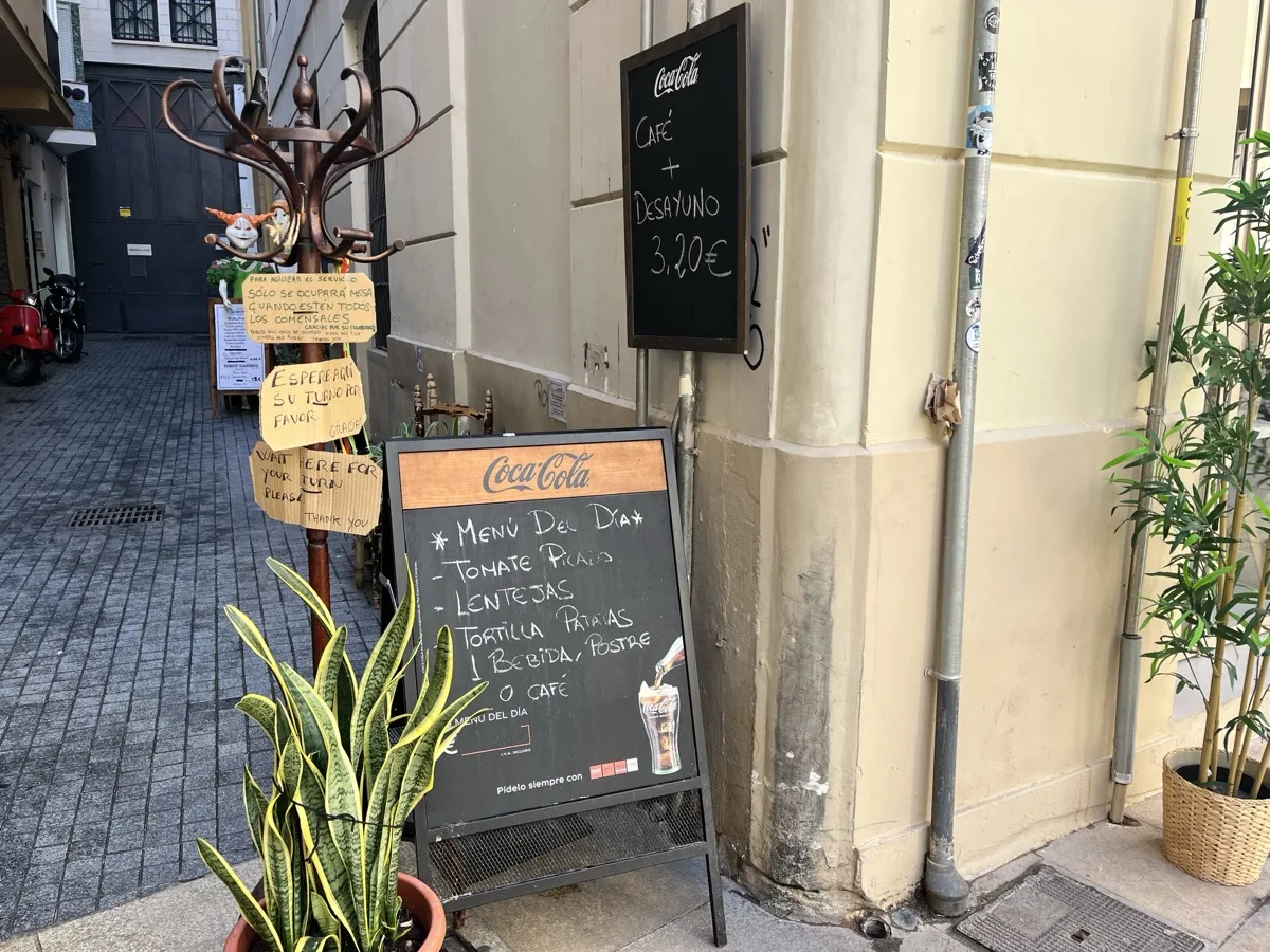 The menú del día chalkboard outside La Recova in Málaga, listing tomate picado, lentejas and tortilla de patatas with a drink, dessert or coffee