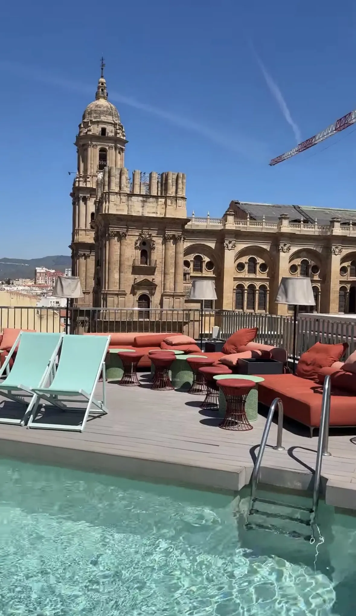 The rooftop pool at La Terraza Molina Lario, mint deckchairs and terracotta loungers on the deck and Málaga Cathedral's tower and unfinished second tower right behind the railing