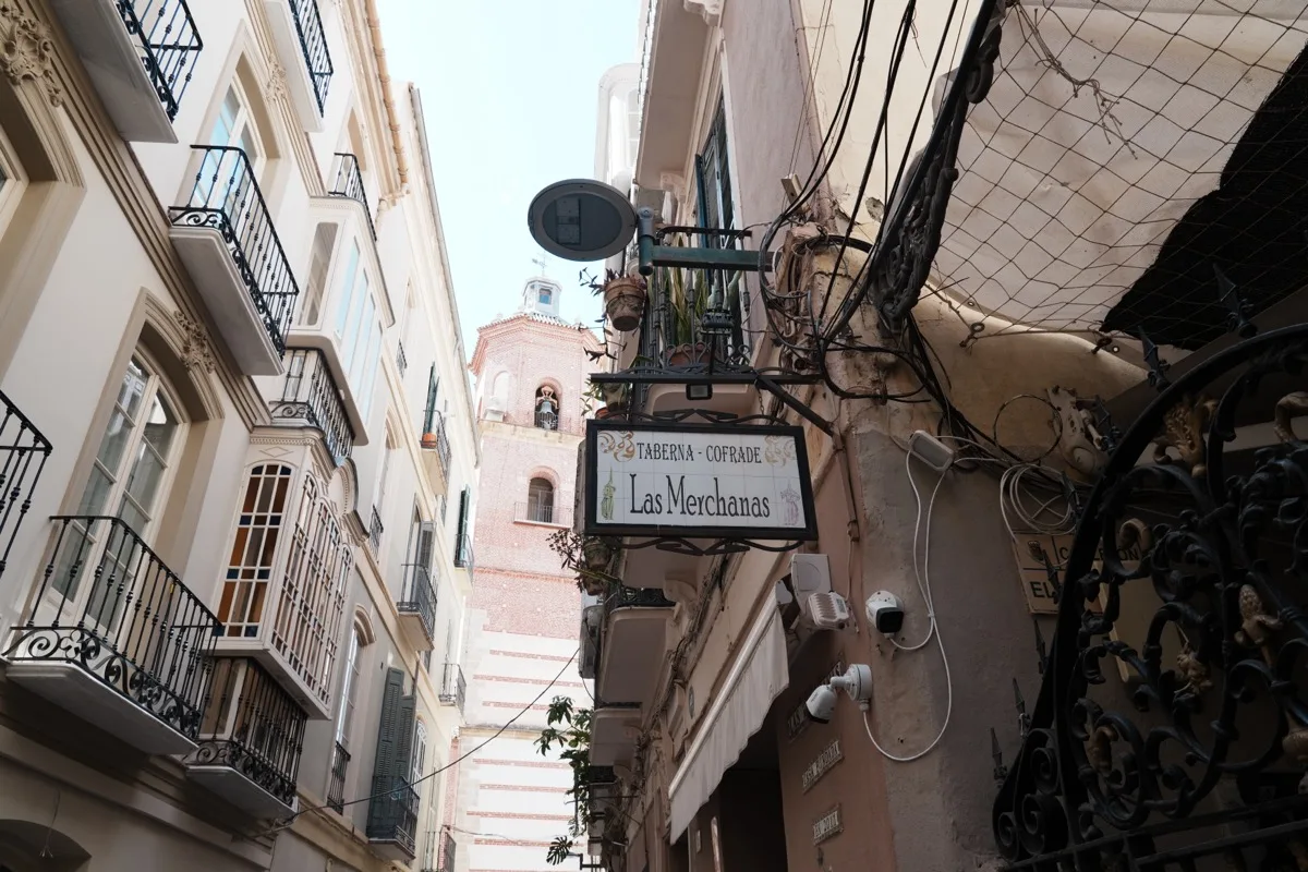 The Taberna Cofrade Las Merchanas sign hanging over narrow Calle Mosquera, a church tower rising at the end of the street