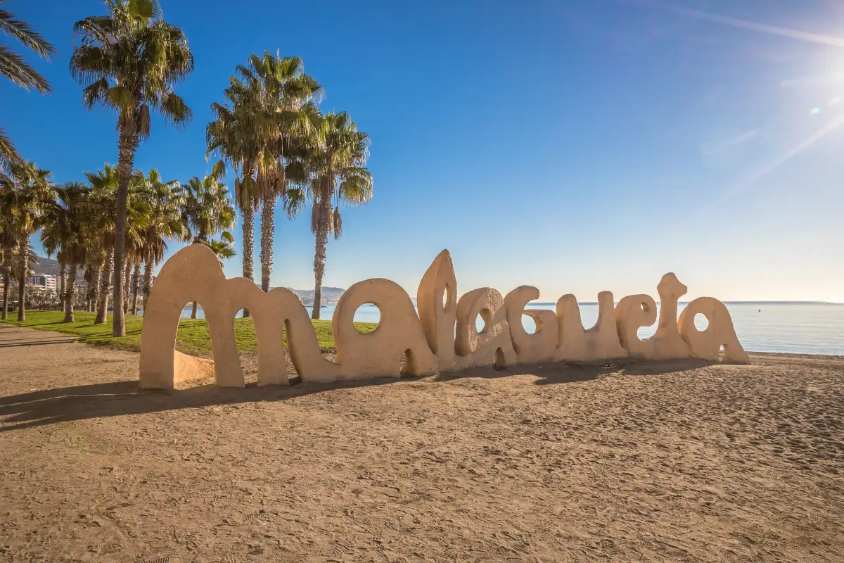 The Malagueta letters sign on the sand at La Malagueta beach in Málaga, with palm trees behind