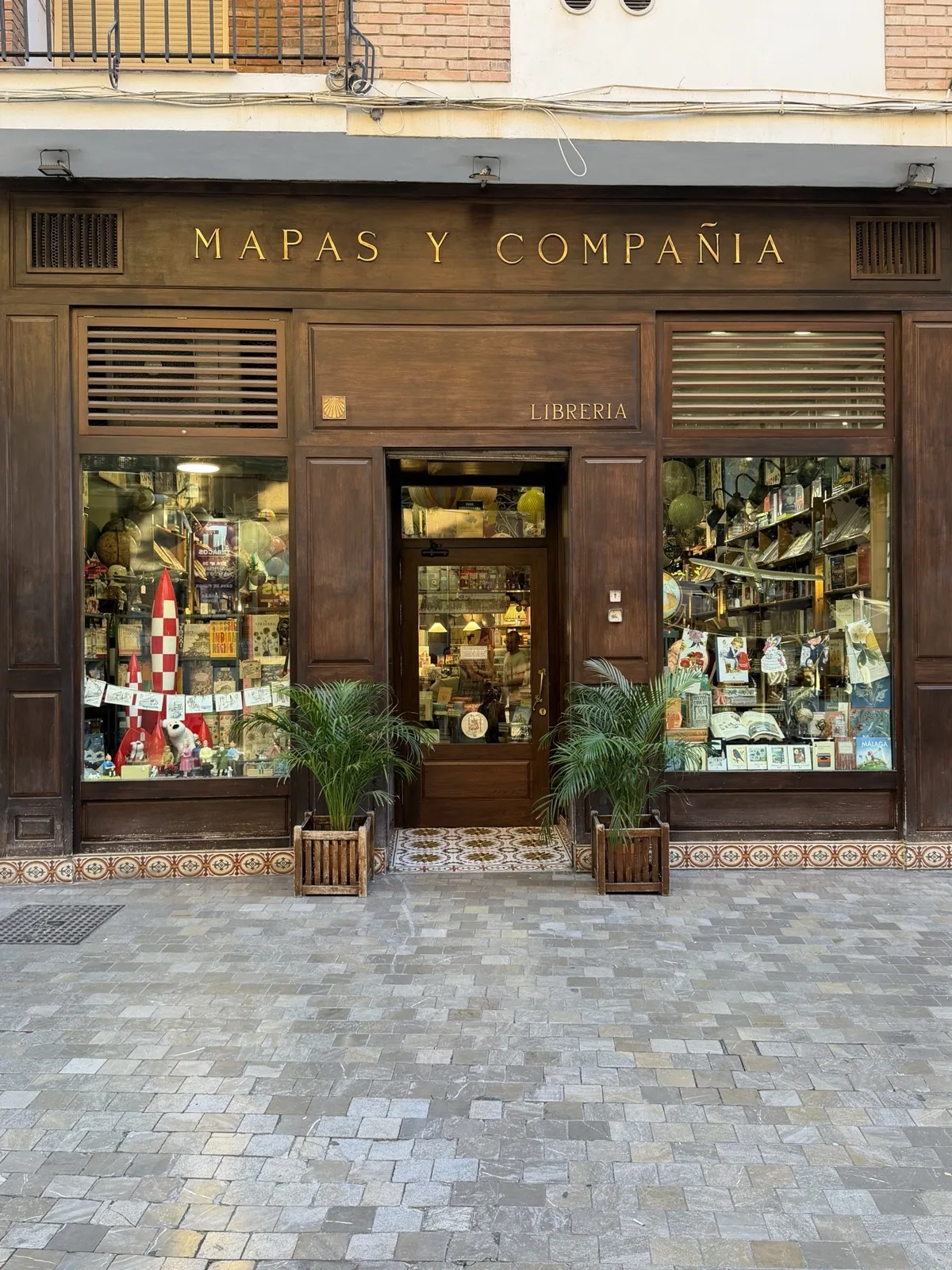 Mapas y Compania storefront in Malaga, wood facade with gold lettering, a Tintin rocket display in the left window and globes visible through the door