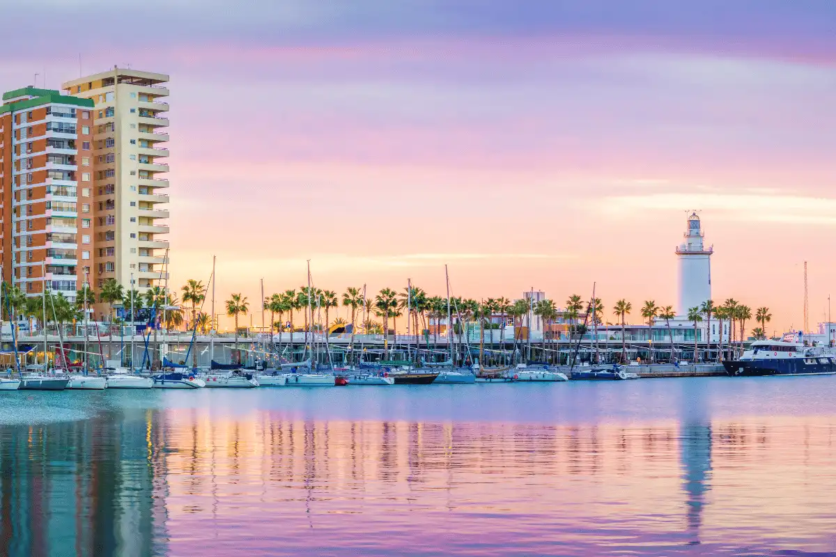 Málaga marina and lighthouse at sunset with sailboats reflected in calm water