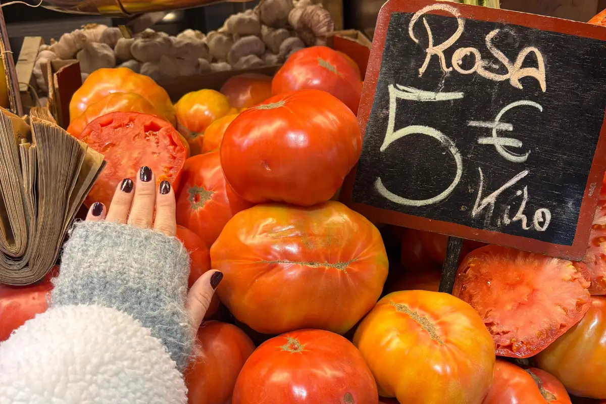 Woman picking up a Rosa variety tomato at a market stall in Málaga, priced at 5 euros per kilo