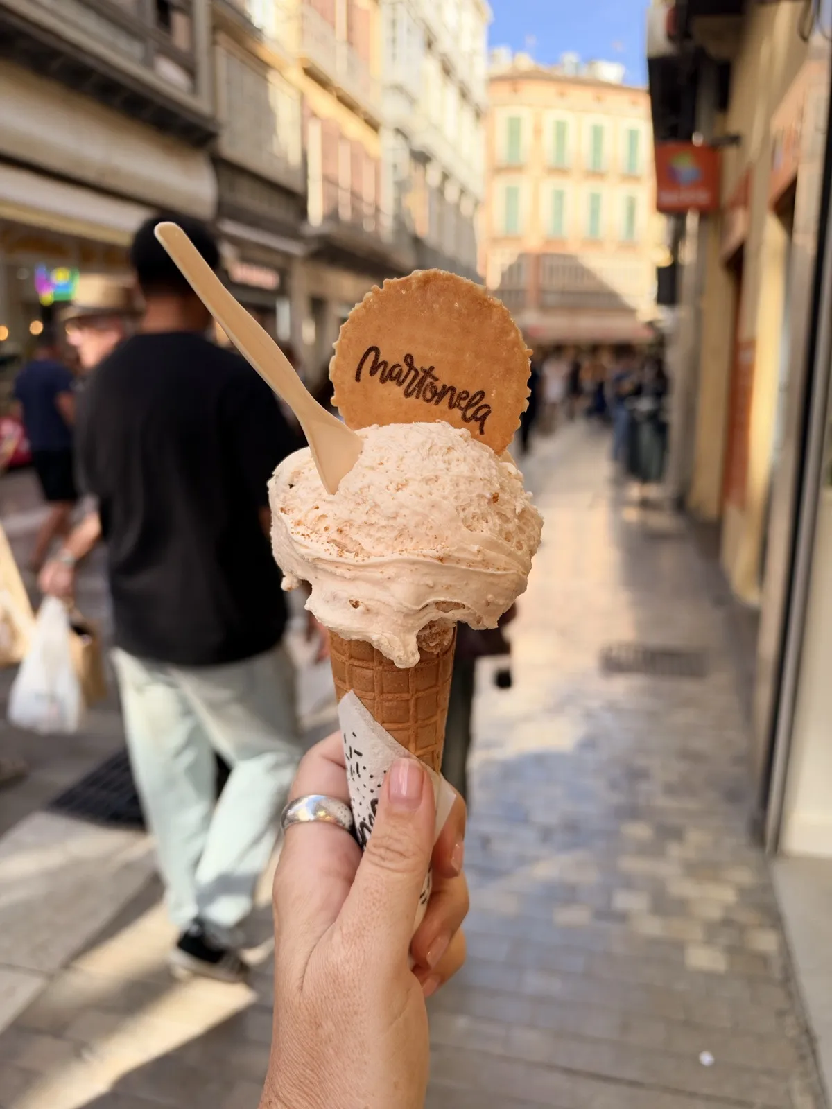 A Martonela cone of Málaga-flavour ice cream held up on a pedestrian street in the old town