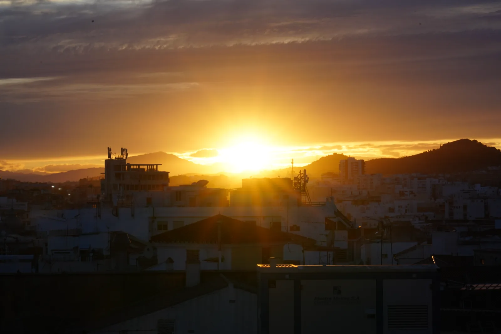 The sun dropping behind the mountains west of Málaga, seen across the old town rooftops from La Terraza Molina Lario