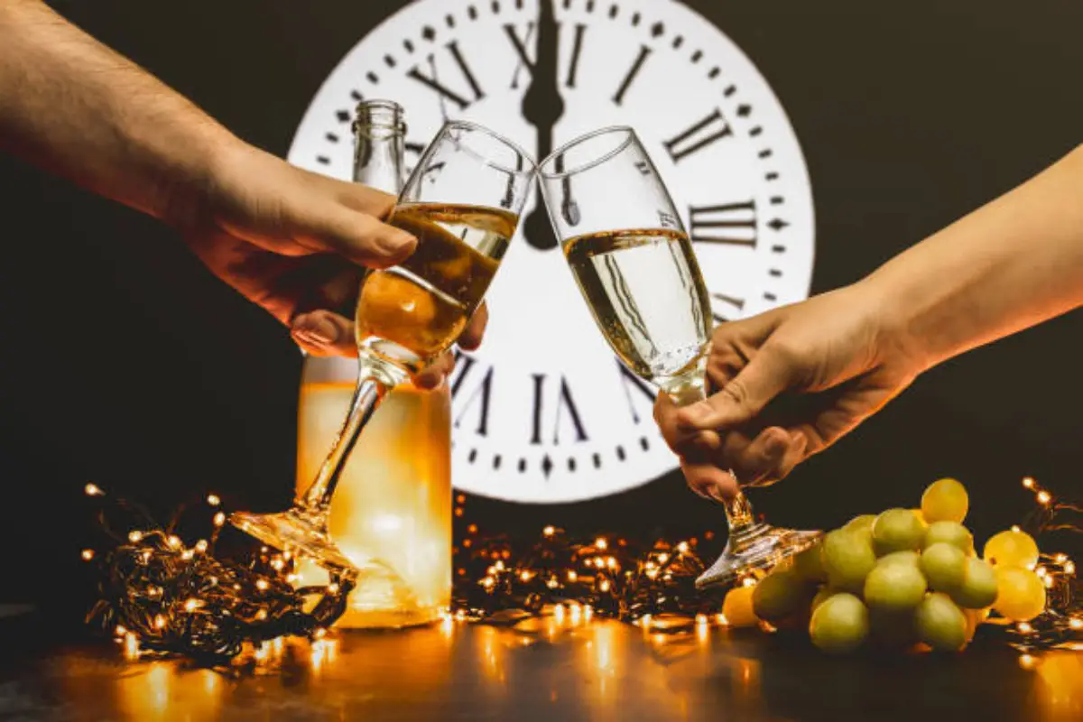 Two people clinking champagne glasses at midnight with twelve grapes on the table