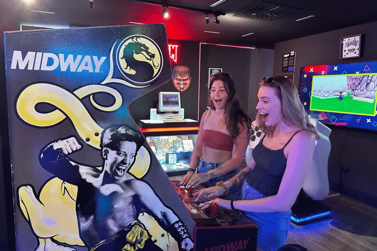 Two women shouting with excitement as they play a Midway Mortal Kombat arcade cabinet at the OXO Museum in Málaga