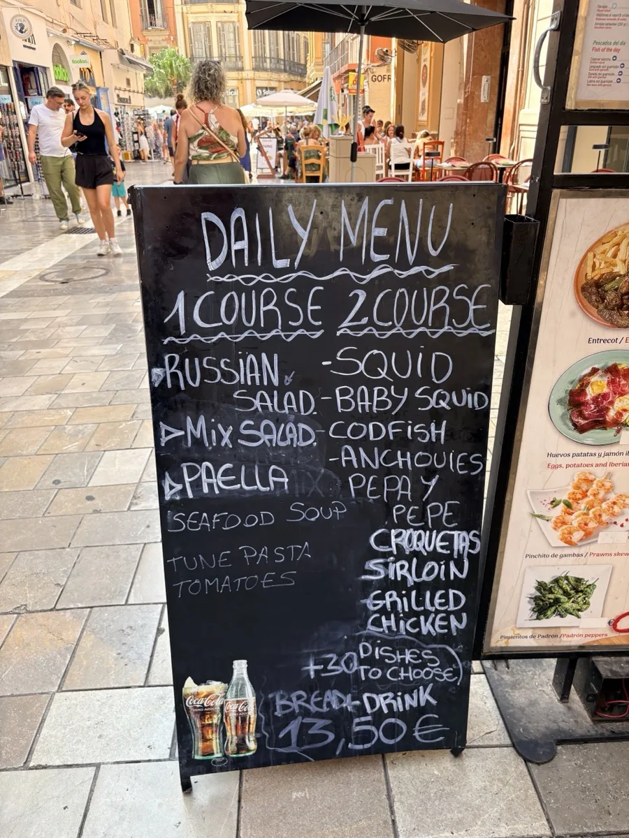 The daily menu board outside Pepa y Pepe in Málaga, listing courses in English with bread and a drink for €13.50