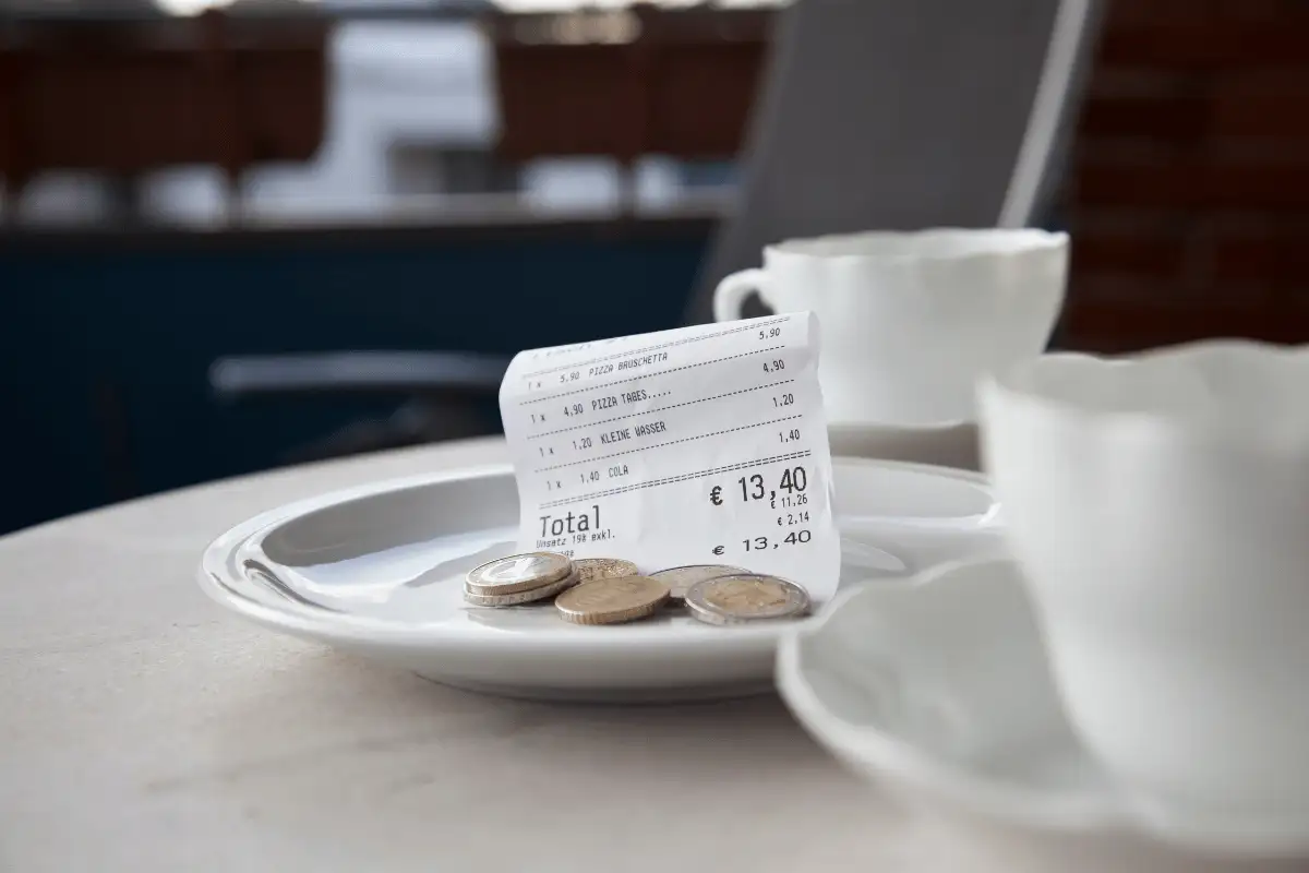 Coffee saucer with a restaurant bill and euro coins on a cafe table