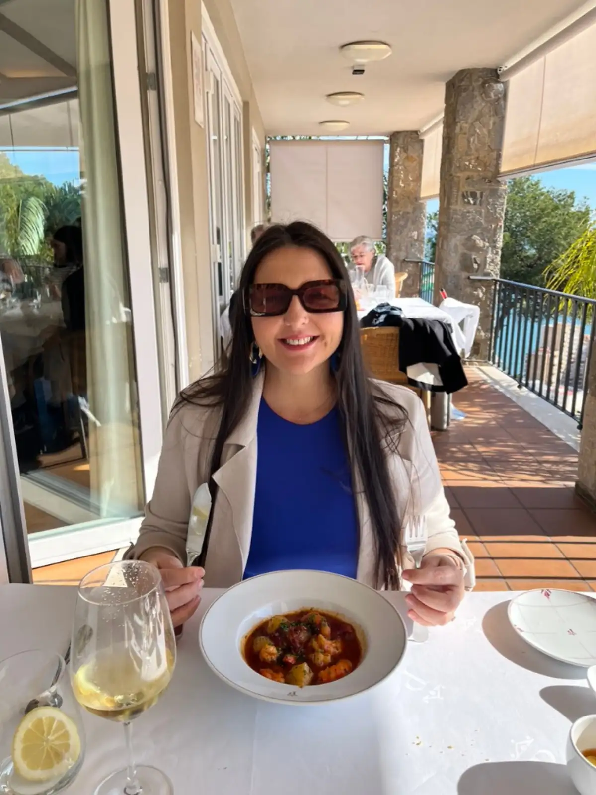 Heidi at a white-tablecloth table on the Parador's covered terrace, a bowl of seafood stew and a glass of white wine in front of her