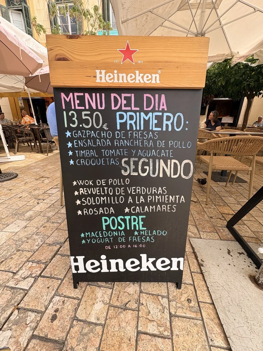 The chalkboard menú del día at Ritas Resto Bar in Málaga, listing primero, segundo and postre for €13.50, served 12:00 to 16:00