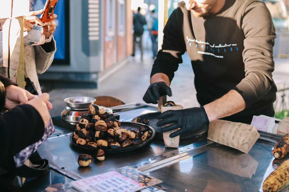 Street vendor wrapping a paper cone of roasted chestnuts for a customer