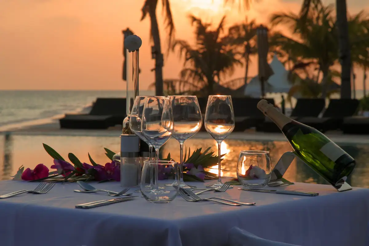 Candlelit table for two with champagne and flowers set beside the sea at sunset