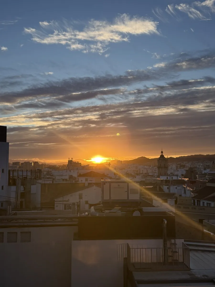 Sun setting low over Málaga's rooftops with the cathedral tower in the distance