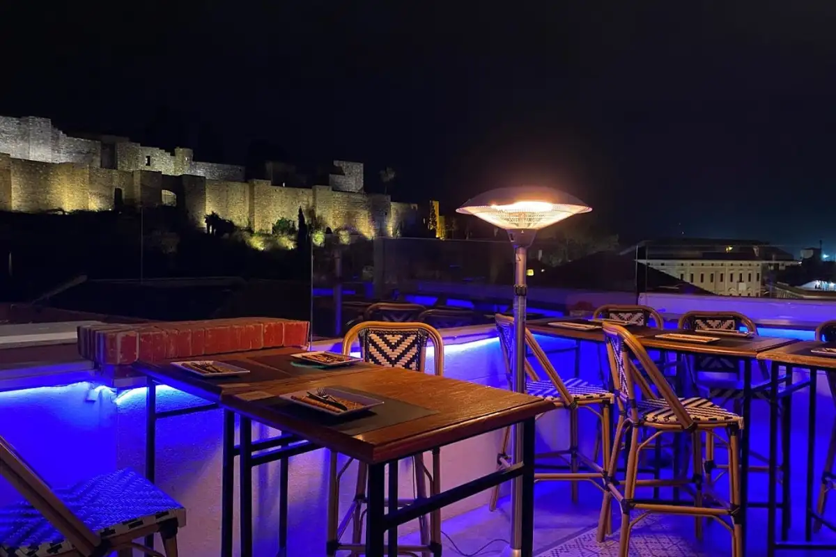 Rooftop terrace bar at night overlooking the illuminated Alcazaba in Malaga