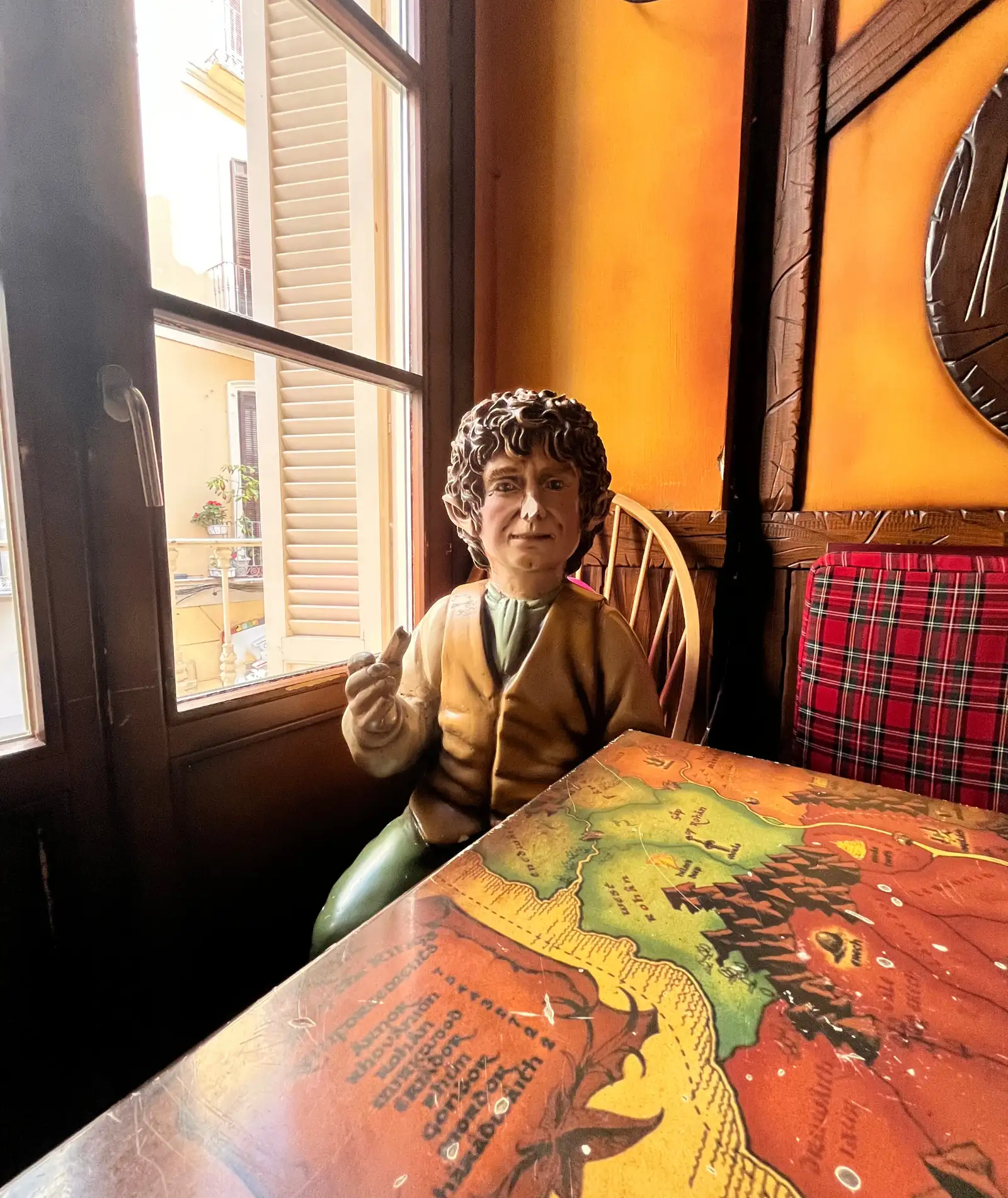 The life-sized wooden hobbit sitting at his window table inside Sala Premier, a map of Middle-earth painted on the tabletop
