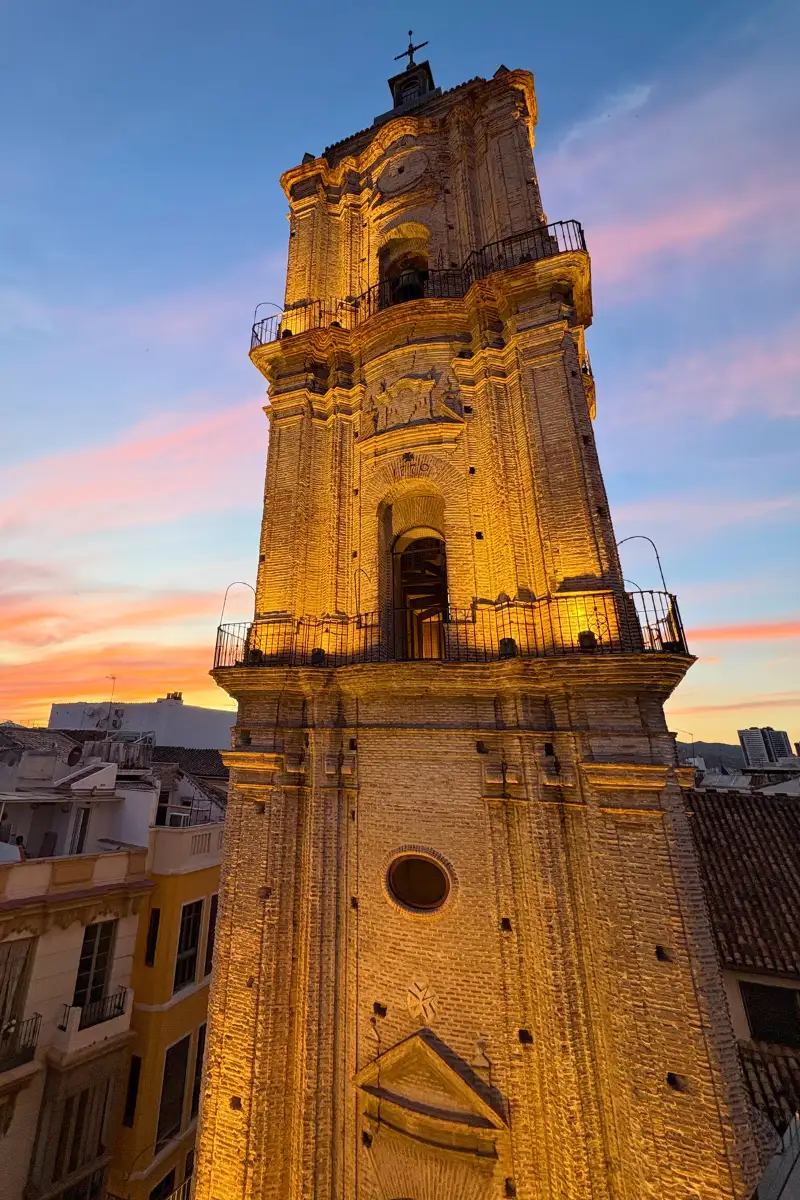 San Juan church bell tower lit up at golden hour, viewed from a rooftop bar in Málaga