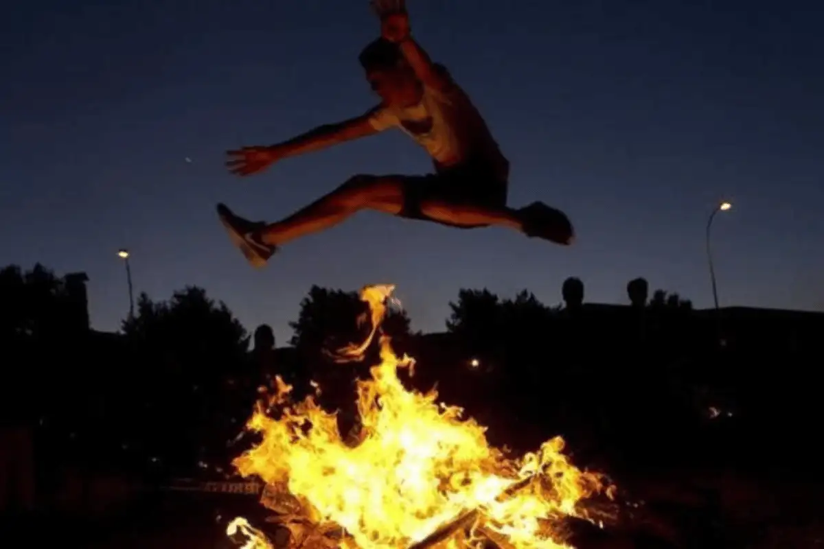 People jumping over a beach bonfire at night during Noche de San Juan in Malaga