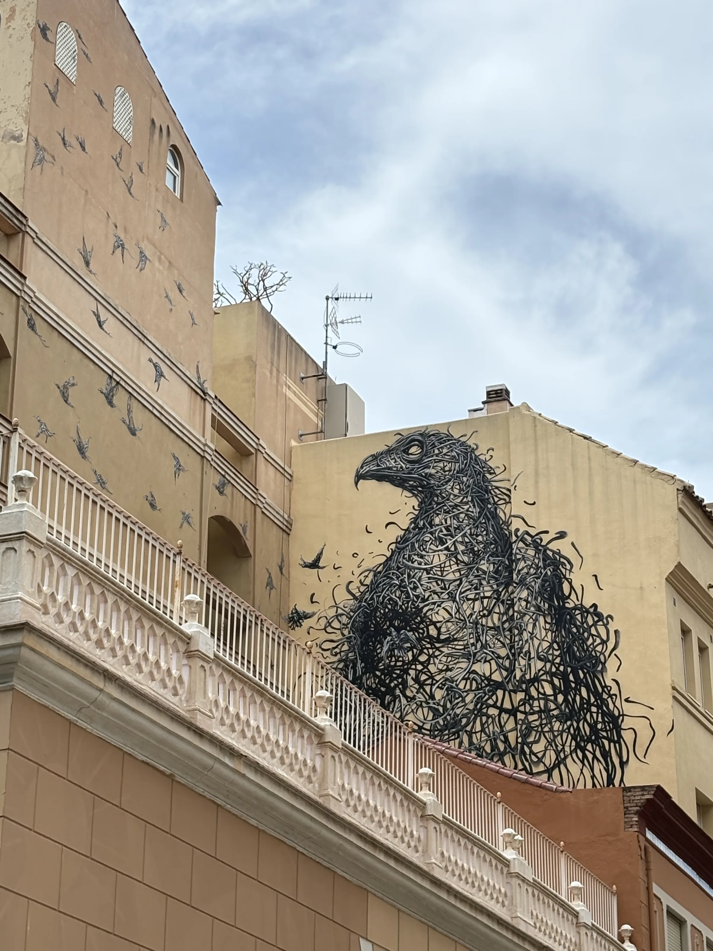 A large mural in Malaga's Soho MAUS district of a bird woven from twisting black lines, with smaller birds bursting free from its body