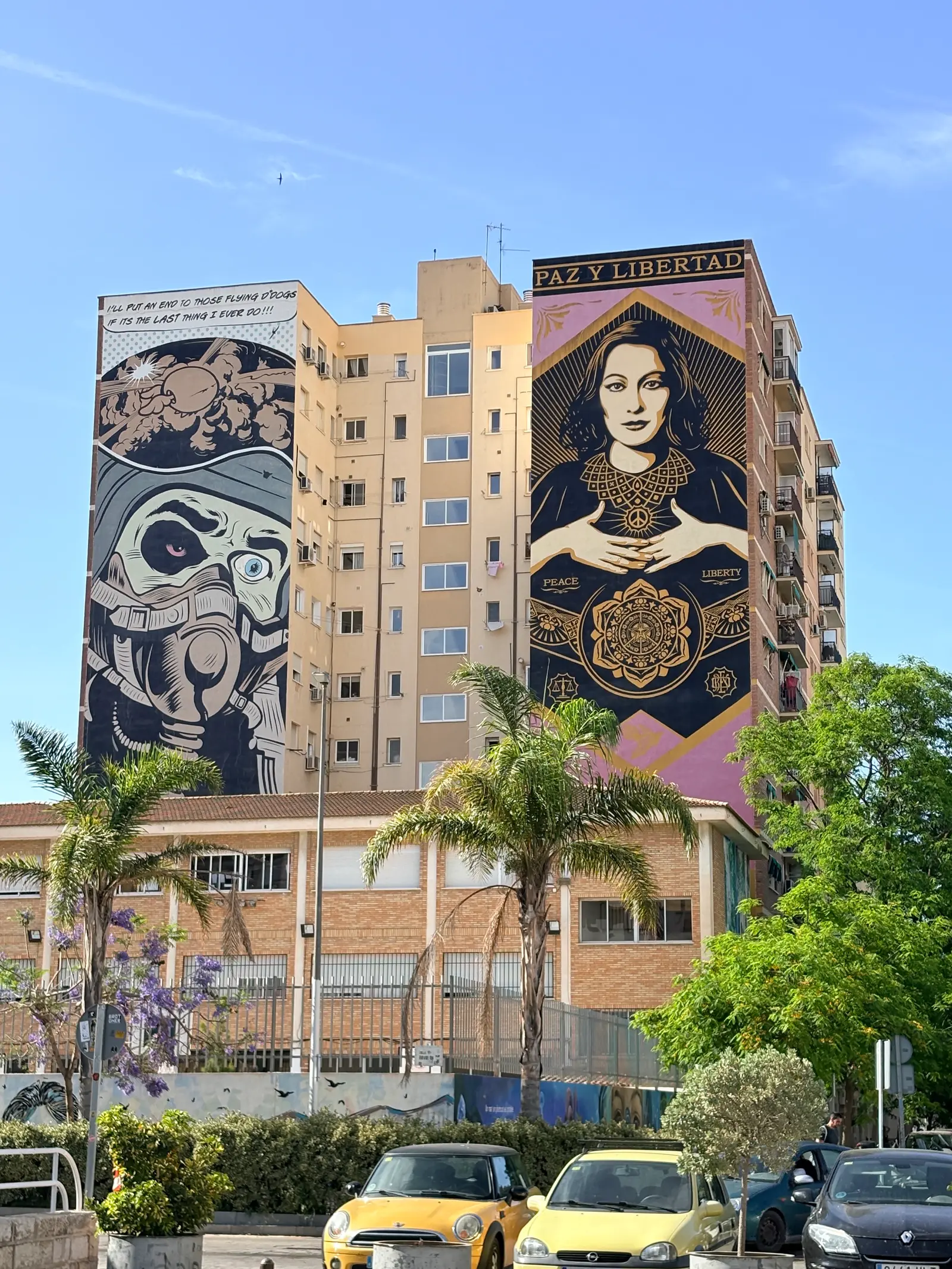 Two large street art murals painted on the sides of apartment buildings in Malaga's Soho district, one a comic-style astronaut, the other a portrait titled "Paz y Libertad".