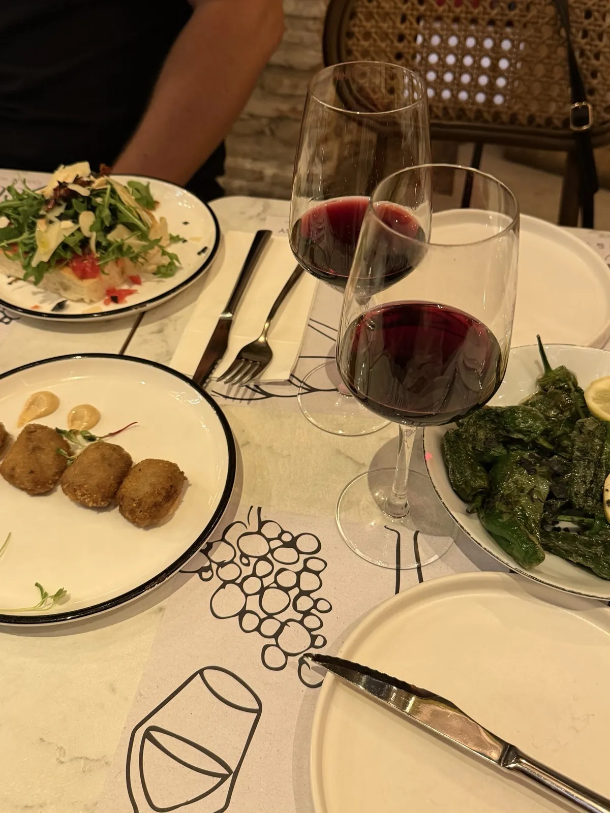 Two glasses of red wine on a table with croquetas and grilled padrón peppers in Málaga