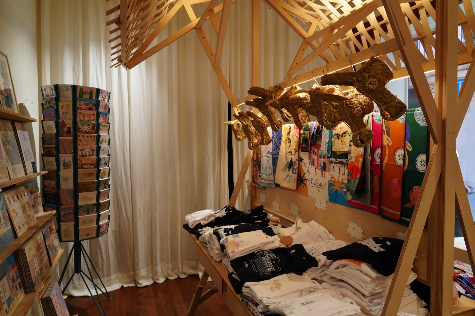 Straw donkey heads hanging from a wooden display at Temporanea Concept Shop in Malaga, next to printed scarves and folded t-shirts