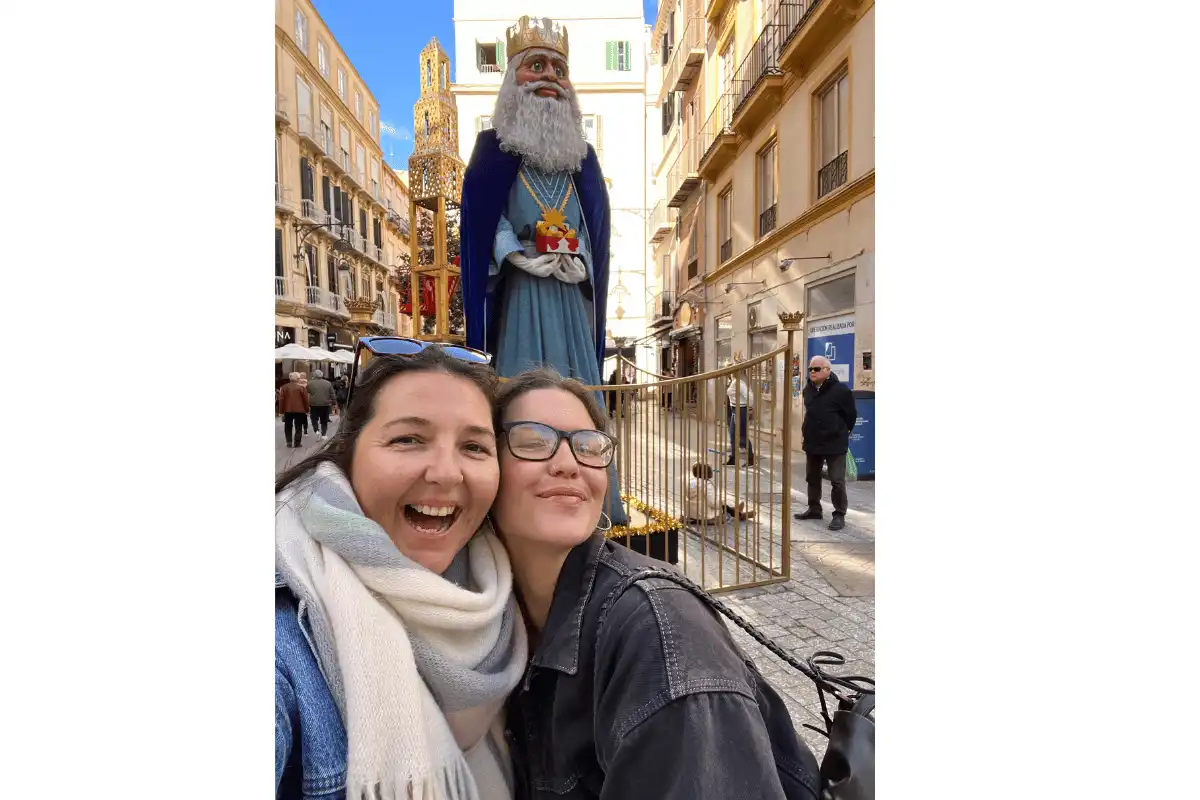 Two women taking a selfie with a giant Three Kings statue near the Roman Theatre in Malaga