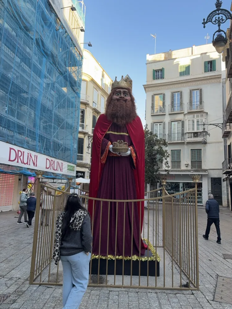 Giant Three Kings statue fenced off on a shopping street in Malaga, with the Druni store and scaffolding behind it